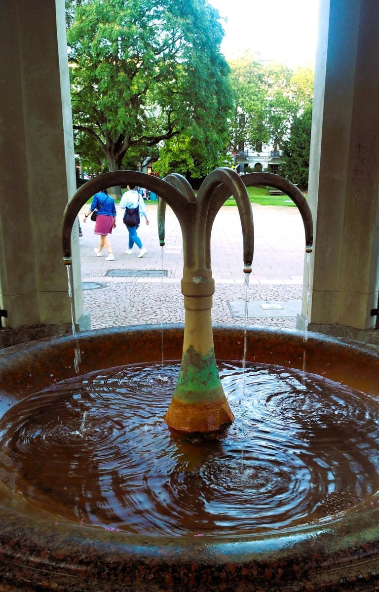 Kochbrunnenspringer Brunnen mit Wasser, das aus einer stilisierten, baumartigen Skulptur fließt.